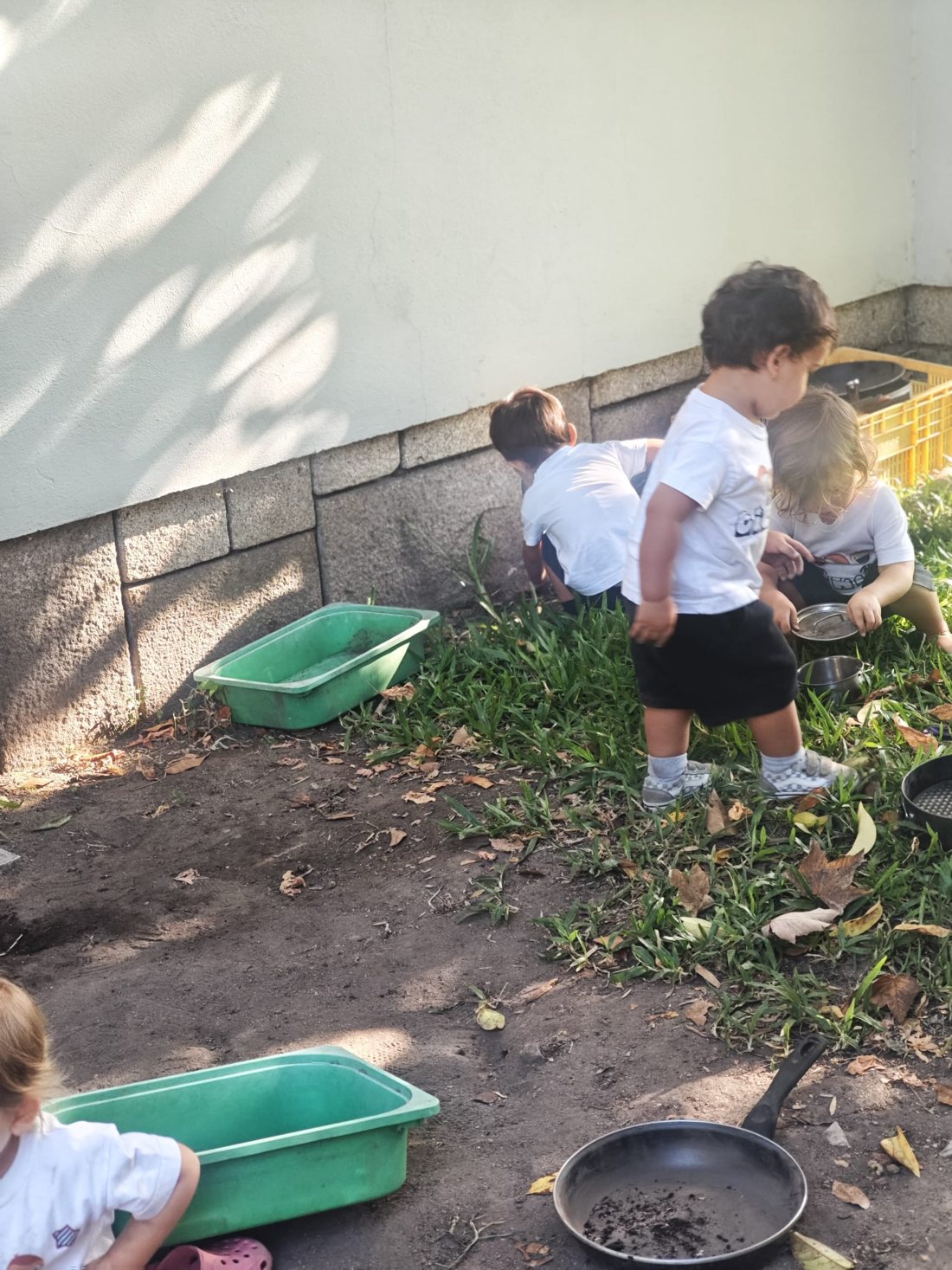 Crianças a brincar junto ao muro do jardim, com alguidares verdes